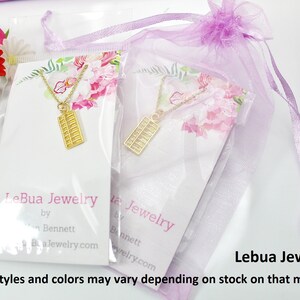 K&ouml;nnte beinhalten: Zwei goldene Abakus-Halsketten in durchsichtiger Plastikverpackung mit rosafarbenem Blumendesign. Die Halsketten sind in einem lila Organzas&auml;ckchen verpackt. Die Verpackung enth&auml;lt den Text "LeBua Jewelry by Bennett Bua.Jewelry.com" und "Lebua Jewelry&trade; *Geschenkbeutel-Stile und -Farben k&ouml;nnen je nach Lagerbestand variieren**"