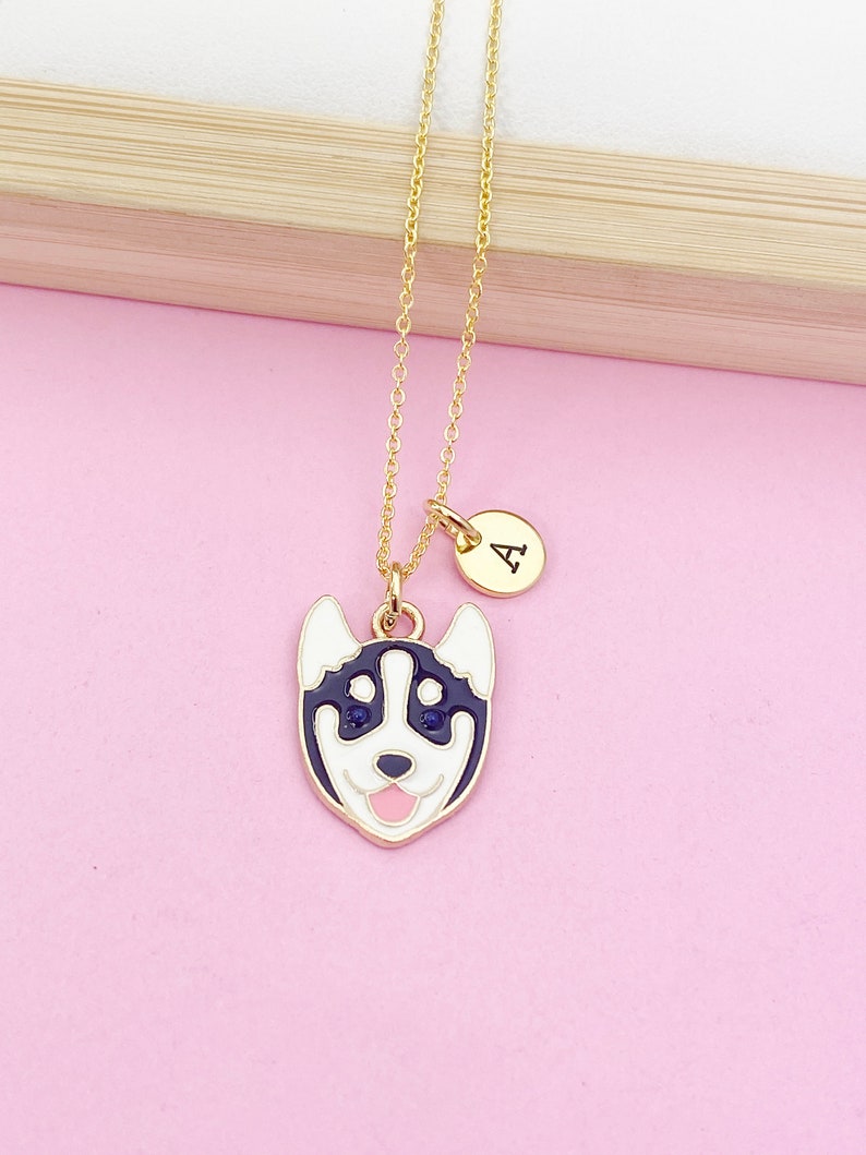 May include: A gold chain necklace with a charm of a cartoon husky dog's face and a small round charm with the letter 'A' on it.