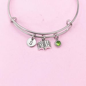 May include: A silver charm bracelet with three charms: a book charm, a green crystal charm, and a charm with the letter "S".