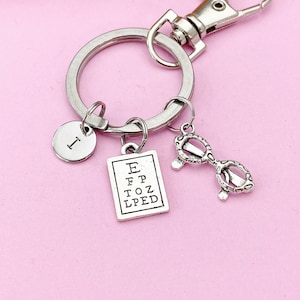 May include: Silver keychain with a letter I charm, a small eye chart charm with the letters E, FP, TOZ, and LPED, and a pair of glasses charm. The charms are attached to a silver ring and a silver lobster clasp.