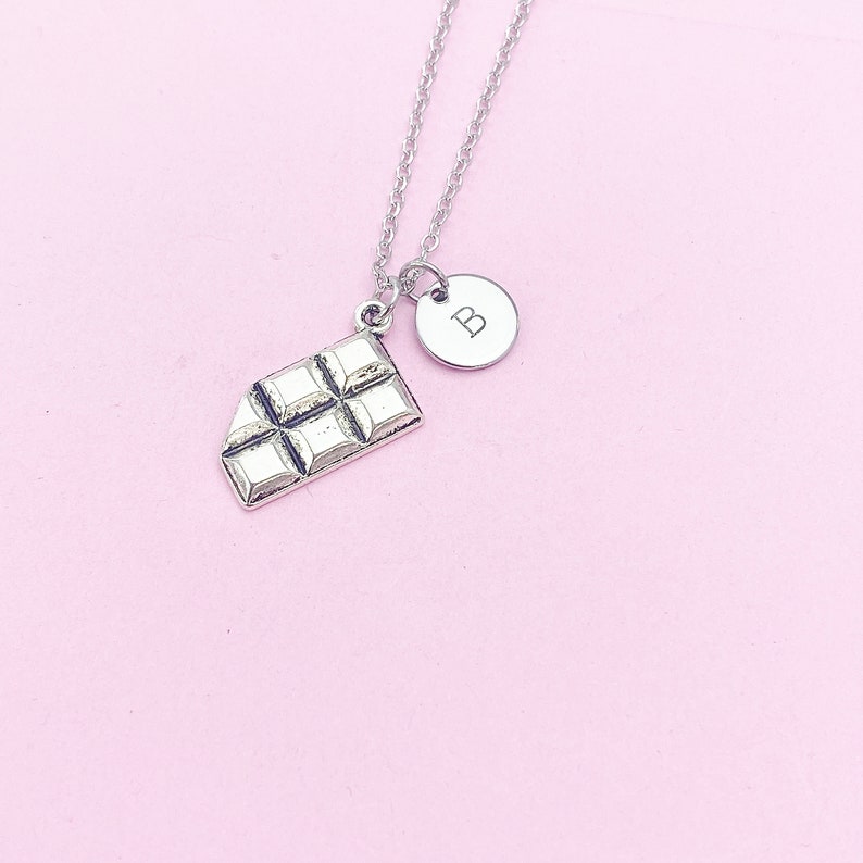 May include: Silver necklace with a chocolate bar charm and a round charm with the letter "B" engraved on it.