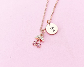 Op de afbeelding: Een ketting van roségoud met een kleine kersenbedel en een ronde hanger met de letter "T" erop gegraveerd.
