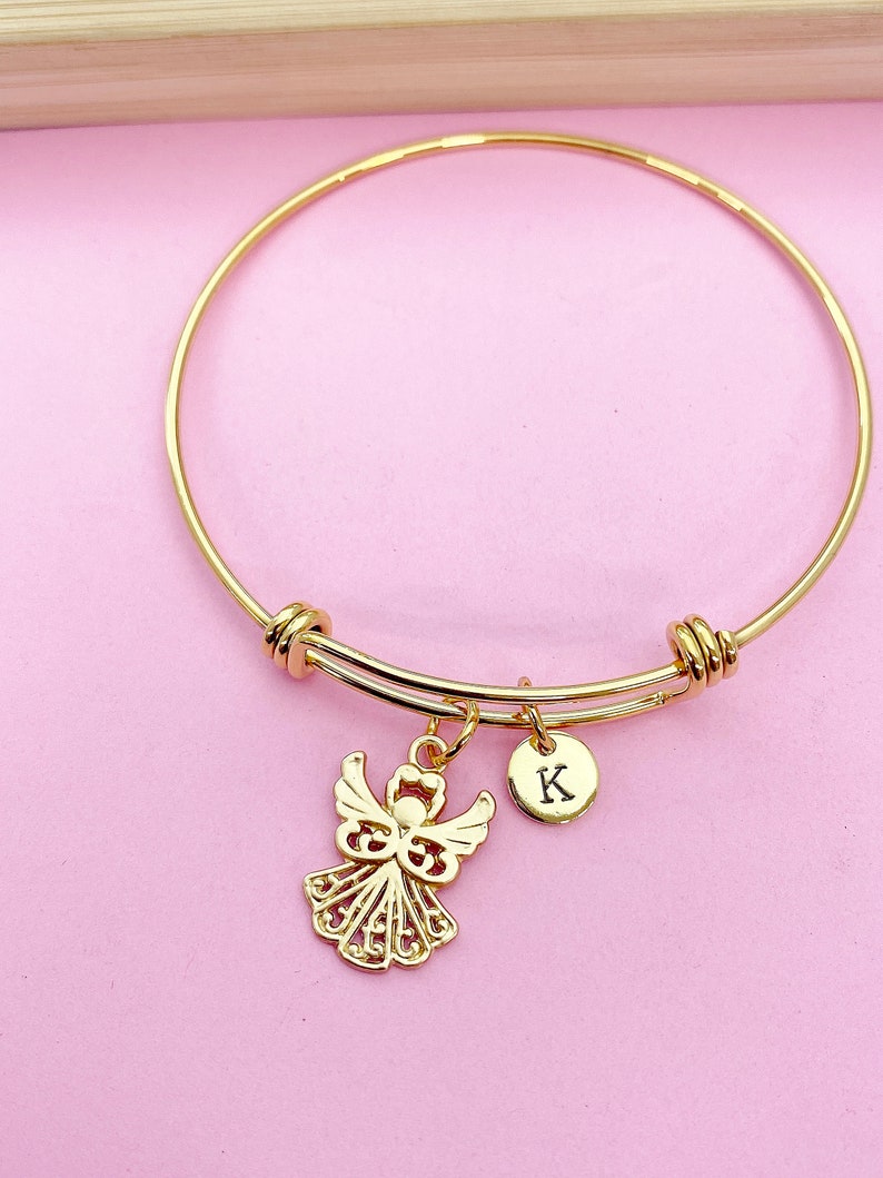 K&ouml;nnte beinhalten: Goldenes Armreif-Armband mit einem Engelsanh&auml;nger und einem kleinen Anh&auml;nger mit dem Buchstaben K.