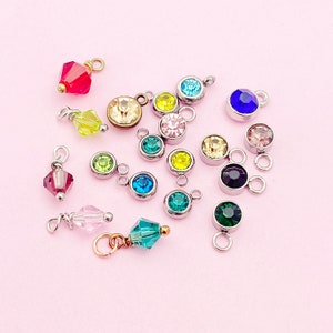 May include: Assortment of colorful crystal charms with silver or gold accents. The charms feature various shapes and sizes of crystals, including round, square, and teardrop.
