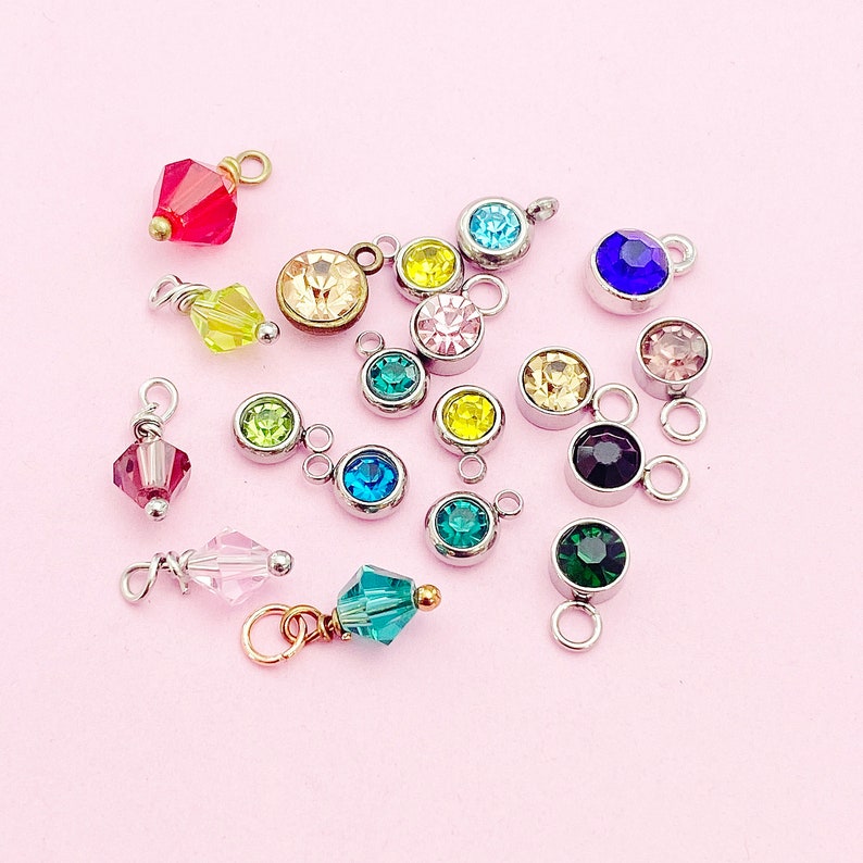 May include: Assortment of colorful crystal charms with silver or gold accents. The charms feature various shapes and sizes of crystals, including round, square, and teardrop.