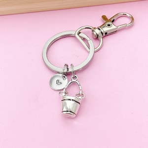 May include: Silver keychain with a small bucket charm and a heart charm. The keychain has a silver split ring and a lobster clasp.