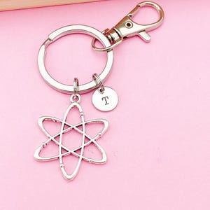 May include: Silver atom keychain with a silver split ring and a silver lobster clasp. The atom charm has a small silver disc with the letter "T" engraved on it.