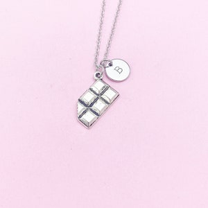 May include: Silver necklace with a chocolate bar charm and a small round charm with the letter "B" on it.