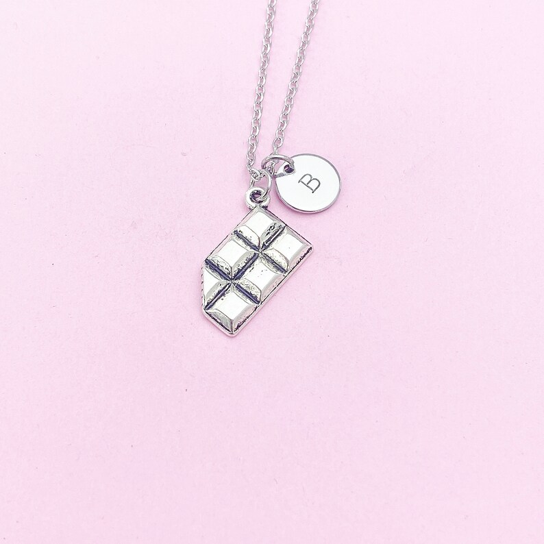May include: Silver necklace with a chocolate bar charm and a small round charm with the letter "B" on it.