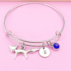 May include: A silver bangle bracelet with a fox charm, a charm with the letter 'S' and a blue crystal charm.