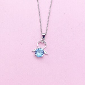 May include: A silver necklace with a blue crystal pendant shaped like a stylized angel with wings.
