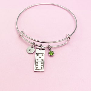 May include: A silver bangle bracelet with three charms: a heart, a domino tile with dots, and a green gemstone.