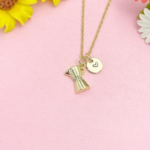 May include: A gold-toned necklace featuring a moka pot pendant and a small circular charm engraved with a heart symbol. The pendant and charm hang from a delicate gold-toned chain, creating a simple and cohesive piece of jewelry.
