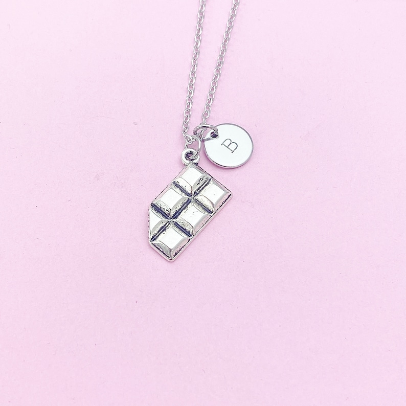 May include: Silver necklace with a chocolate bar charm and a round charm with the letter "B" on it.