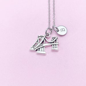 May include: Silver necklace with a charm of the Golden Gate Bridge and a small charm with the letter B.