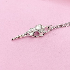 May include: A silver bird skull pendant necklace. The pendant is detailed and has a textured surface. The chain is silver and has a lobster clasp.