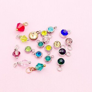 May include: Assortment of colorful crystal charms with silver jump rings. The charms feature various colors, including red, green, blue, yellow, and pink.
