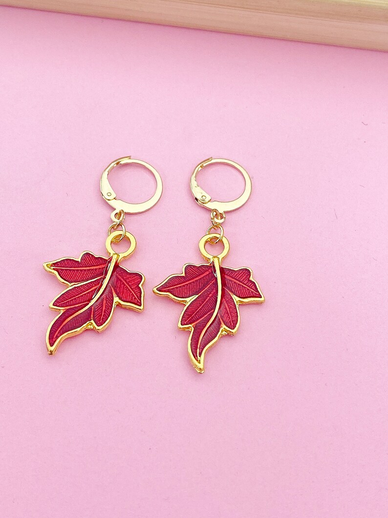 May include: A pair of gold hoop earrings with red leaf charms. The leaves have a detailed design and a glossy finish.