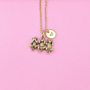May include: Gold necklace with a charm of three monkeys, one covering its eyes, one covering its ears, and one covering its mouth. The charm is attached to a small gold disc with a heart engraved on it.
