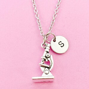 May include: Silver necklace with a small microscope charm and a round charm with the letter "S" on it.