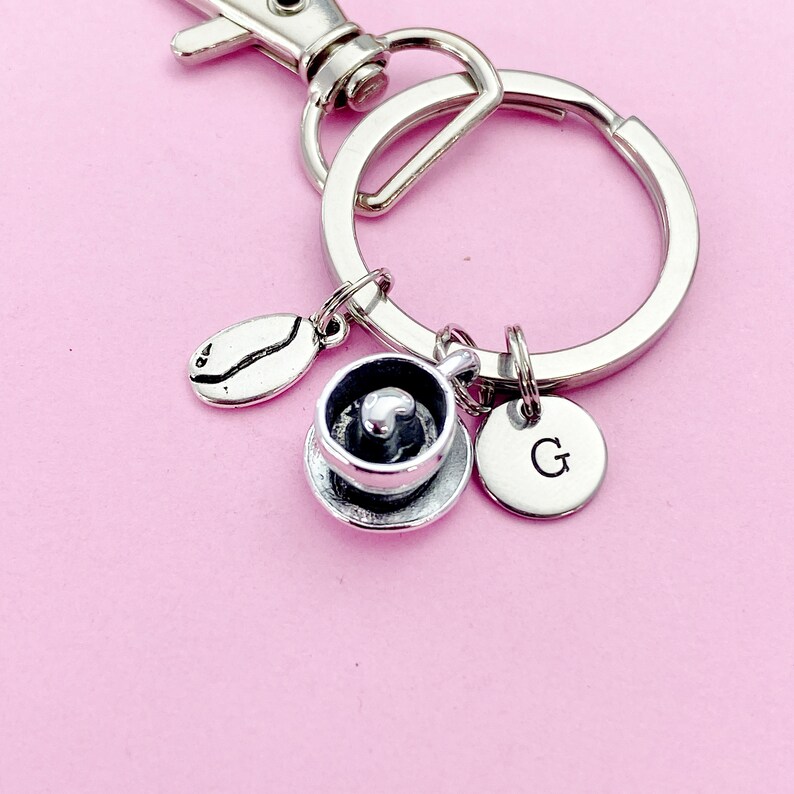 May include: Silver keychain with a coffee cup charm, a coffee bean charm, and a charm with the letter G.