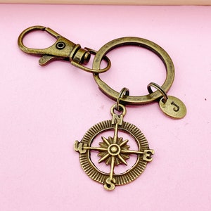 May include: A bronze compass keychain with a round compass charm and a split ring. The compass charm has a star in the center and the letters N, S, E, and W around the edge.