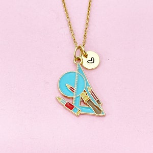 May include: A gold chain necklace with a charm featuring a blue protractor, ruler, pencils, and a red pen. A small gold charm with a heart symbol hangs below the larger charm.
