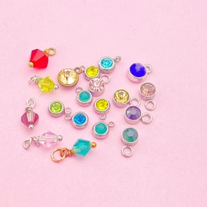 May include: Assortment of colorful crystal charms with silver jump rings. The charms feature various colors including red, yellow, green, blue, and purple.