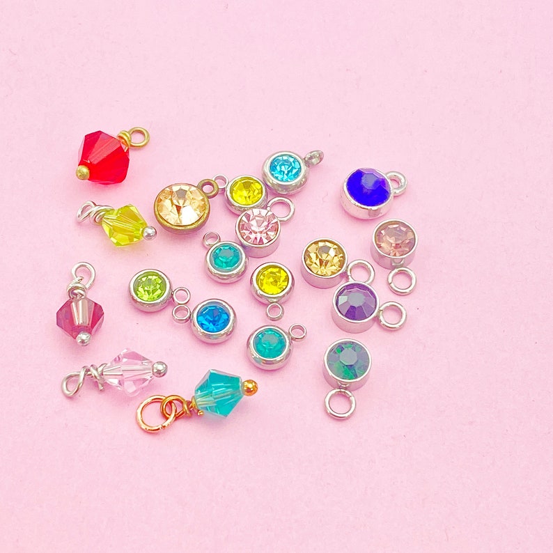 May include: Assortment of colorful crystal charms with silver jump rings. The charms feature various colors including red, yellow, green, blue, and purple.