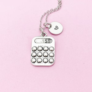 May include: Silver calculator charm necklace with a small heart charm. The calculator charm has a display that reads "123" and a grid of buttons.