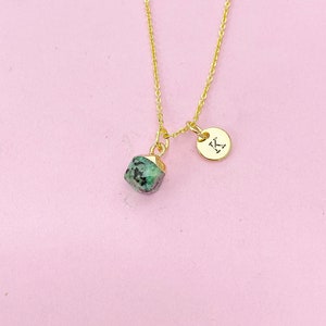 May include: A gold chain necklace with a green gemstone pendant and a small gold charm with the letter "K" on it.