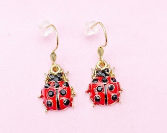 May include: A pair of gold-tone earrings featuring a red and black ladybug design. The ladybugs have black spots and gold accents.