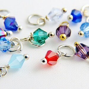 May include: Assortment of colorful crystal beads with silver and gold accents, attached to silver jump rings. The beads are various shapes and sizes, including round, square, and teardrop.