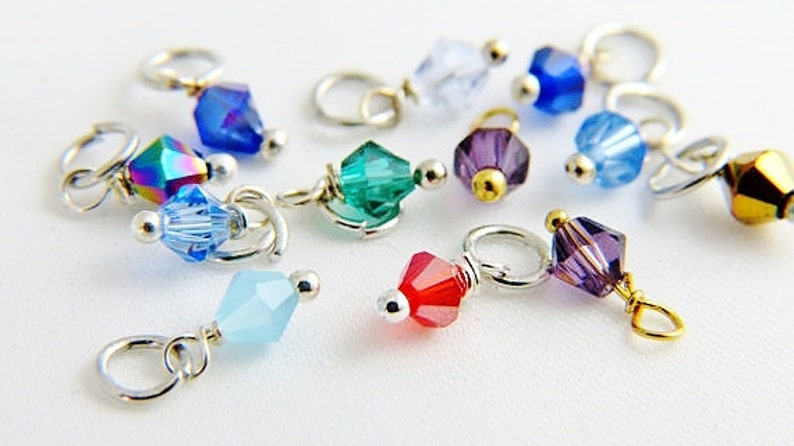 May include: Assortment of colorful crystal beads with silver and gold accents, attached to silver jump rings. The beads are various shapes and sizes, including round, square, and teardrop.
