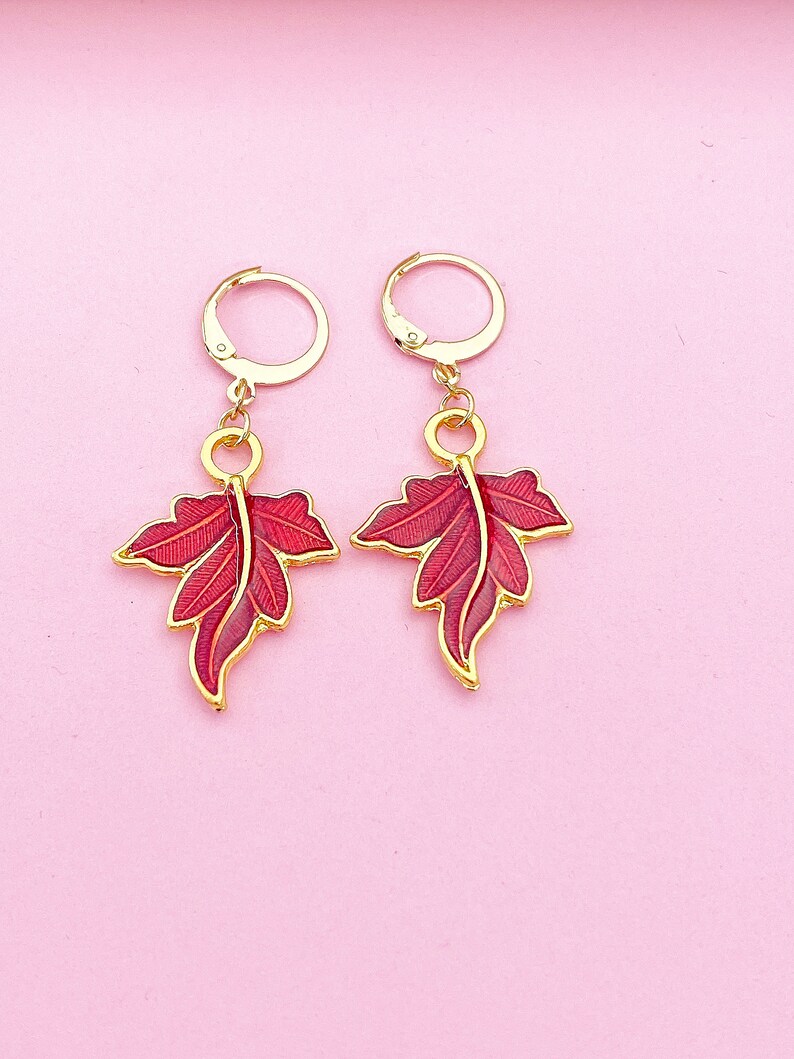 May include: A pair of gold earrings with red leaf-shaped charms. The earrings have a hoop design and are perfect for adding a touch of nature to any outfit.