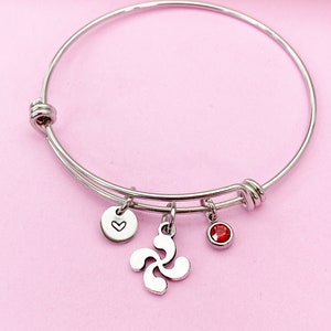 May include: A silver bangle bracelet with three charms: a small heart charm, a red crystal charm, and a silver charm with a swirl design.