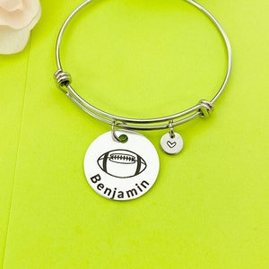 May include: Silver bangle bracelet with a charm featuring a football and the name "Benjamin".