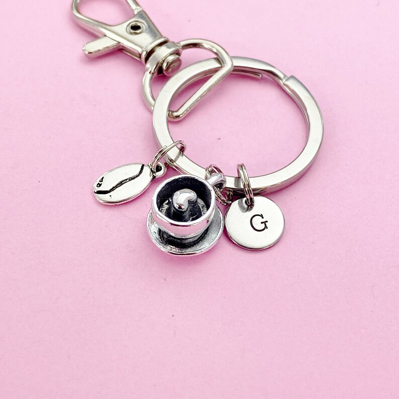May include: Silver keychain with a coffee cup charm, a coffee bean charm, and a charm with the letter G.