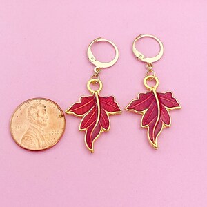 May include: A pair of gold earrings with red enamel leaf designs. The leaves are detailed with gold veins and have a slightly textured surface.