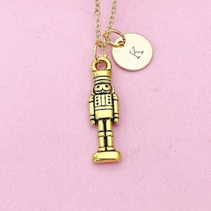 May include: Gold necklace with a gold nutcracker charm and a gold initial charm with the letter K.
