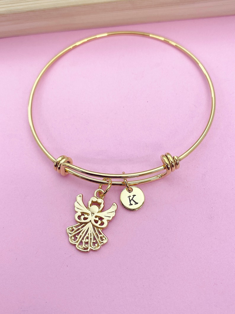 K&ouml;nnte beinhalten: Goldenes Armreif-Armband mit einem Engelsanh&auml;nger und einem kleinen runden Anh&auml;nger mit dem eingravierten Buchstaben "K".