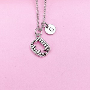 May include: Silver necklace with a charm of a set of fangs and a small round charm with the letter 'C' on it.