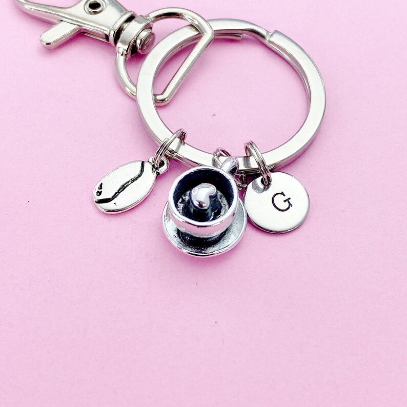 May include: Silver keychain with a coffee cup charm, a coffee bean charm, and a charm with the letter G.