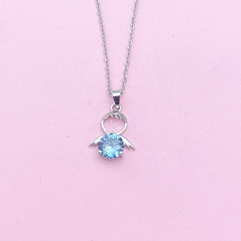 May include: A silver necklace with a blue gemstone pendant shaped like a stylized person with outstretched arms.