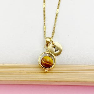 May include: Gold necklace with a spinning tiger's eye stone pendant and a small gold charm with the letter 'L' on it.