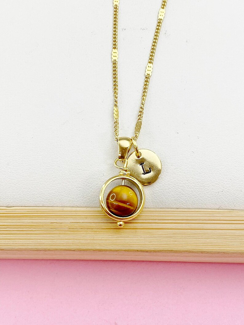 May include: Gold necklace with a spinning tiger's eye stone pendant and a small gold charm with the letter 'L' on it.