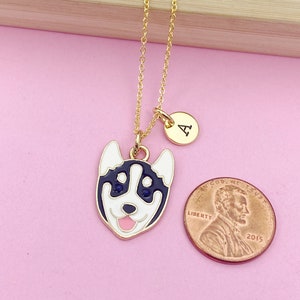 May include: Gold chain necklace with a charm of a cartoon husky dog with blue eyes and a pink tongue. The charm is attached to a gold circle with the letter "A" on it.