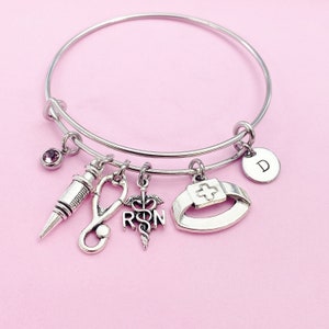 May include: Silver charm bracelet with a variety of charms including a stethoscope, a syringe, a nurse's cap, and a medical symbol with the letters "RN". The bracelet also has a small pink crystal charm and a charm with the letter "D".