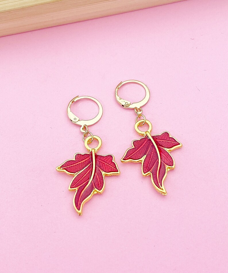 May include: A pair of gold earrings with red leaf-shaped charms. The leaves have a detailed design and a glossy finish.
