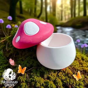 Könnte beinhalten: Ein rosa pilzförmiger Behälter mit weißen Punkten und einem passenden Deckel. Der Behälter ist weiß und rund. Das Bild ist in einer natürlichen Umgebung im Freien mit Schmetterlingen und dem Mossmaid Grove-Logo aufgenommen.